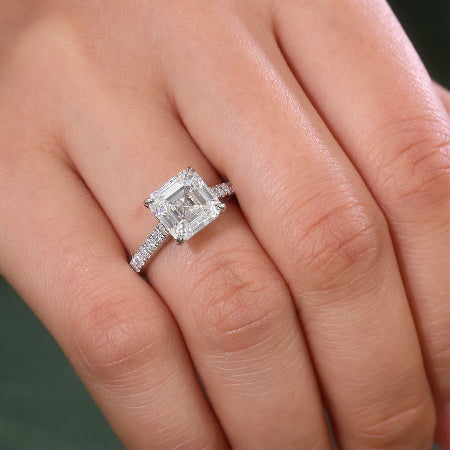 Emerald cut moissanite engagement ring in solid 14K white gold featuring a hidden baguette halo and pavé diamond accent band