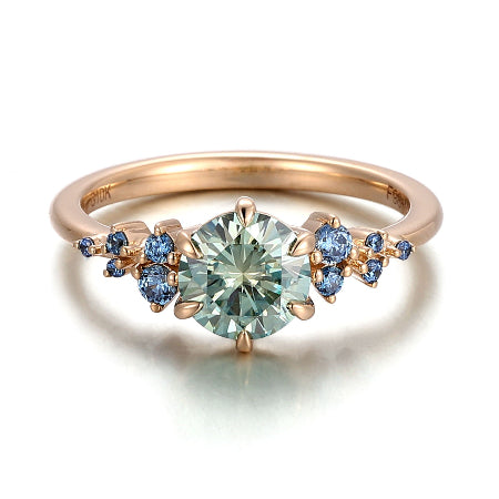round green moissanite engagement ring in solid 14k rose gold featuring blue sapphire cluster side stones and a nature-inspired setting.
