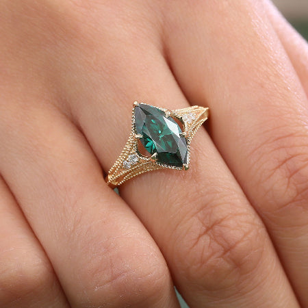 green marquise cut moissanite engagement ring in yellow gold with vintage split shank and accent diamonds worn on finger.