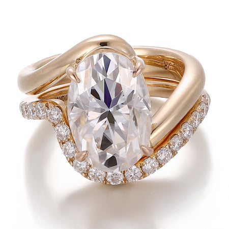 Oval cut moissanite bridal ring set featuring a twisted bypass engagement ring with a matching curved pavé diamond wedding band in solid rose gold.