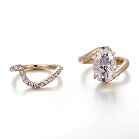 Oval cut moissanite bridal ring set featuring a twisted bypass engagement ring with a matching curved pavé diamond wedding band in solid rose gold.