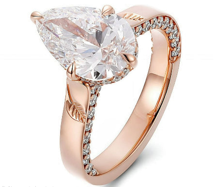Pear cut moissanite engagement ring in solid 14K rose gold featuring pavé accents and engraved leaf details in a nature-inspired solitaire setting.