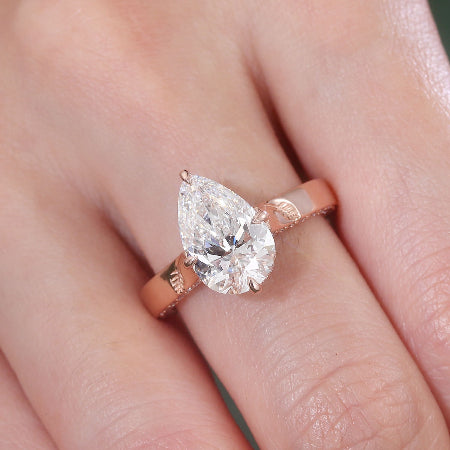pear cut moissanite engagement ring in solid 14k rose gold featuring pavé accents and engraved leaf details in a nature-inspired solitaire setting.