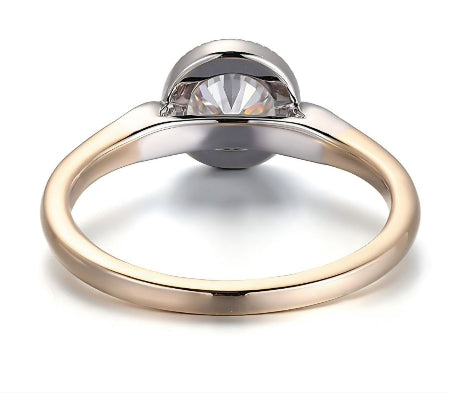 Round bezel set moissanite engagement ring with a two-tone solid gold band and diamond side accents. Modern minimalist solitaire ring for women.