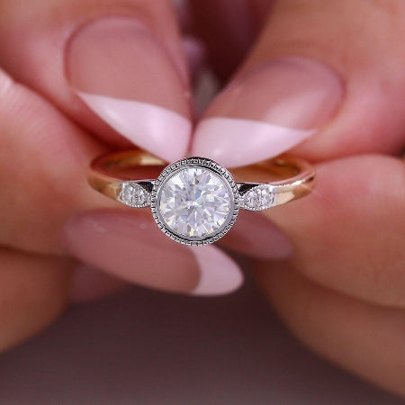 round bezel set moissanite engagement ring with a two-tone solid gold band and diamond side accents. modern minimalist solitaire ring for women.